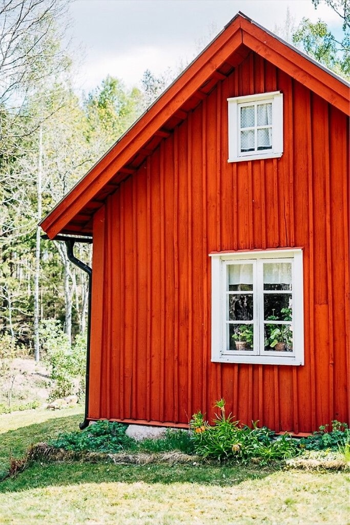 Röd träbyggnad med vita fönster i grön miljö