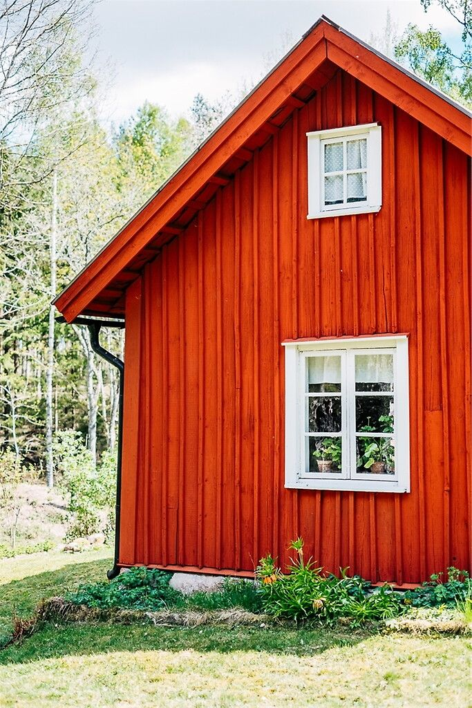 Röd träbyggnad med vita fönster i grön miljö
